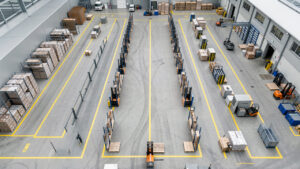 Vue aérienne d’un atelier industriel organisé avec des zones logistiques distinctes, des équipements de manutention et des flux de circulation clairement structurés.